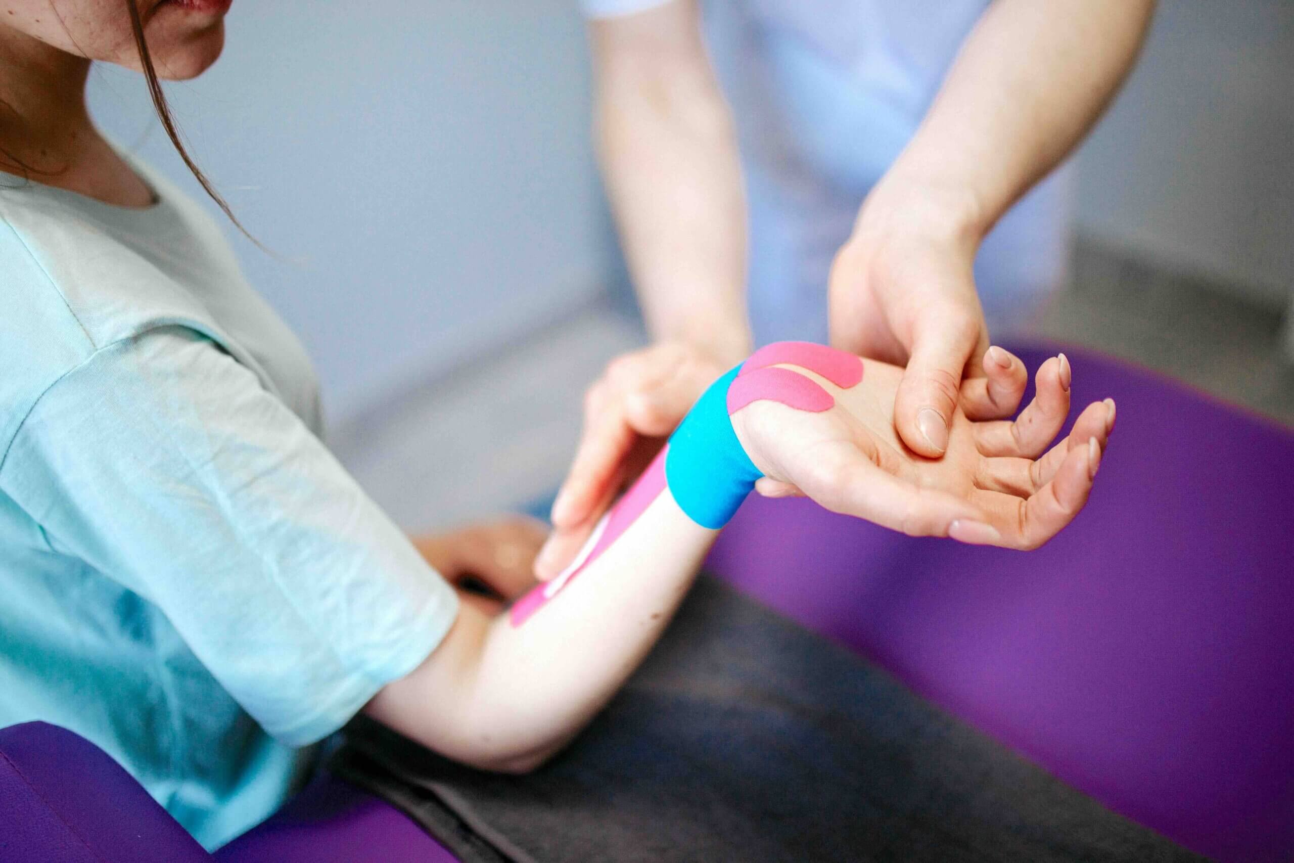 Health professional applying kinesiology tape to a patient's wrist, representing the health and fitness clients Jess Creatives supports with website design for healthcare professionals